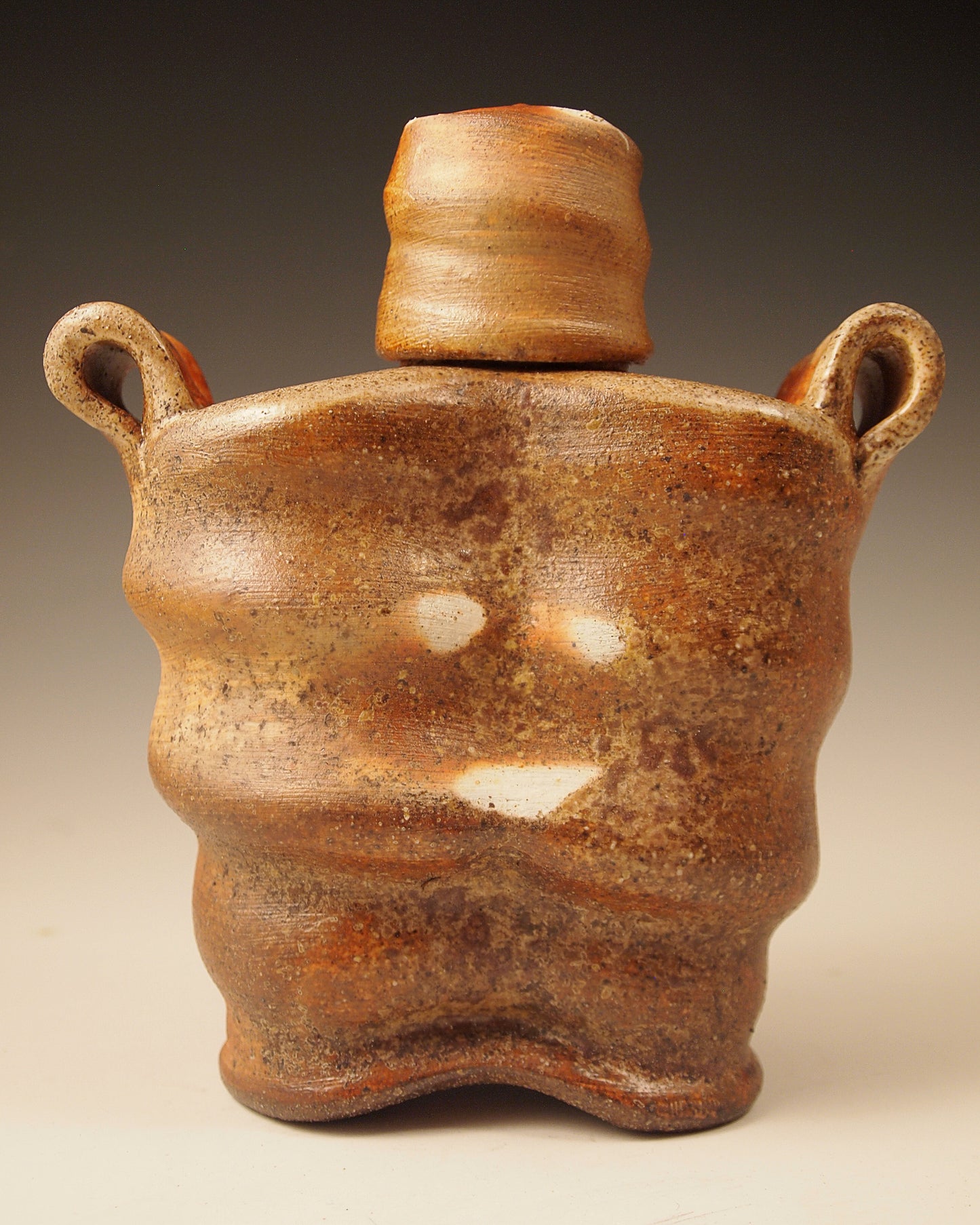 Wood-fired stoneware whiskey flask with liner glaze. Handmade Pottery.  Unique design, yet functional. 7" tall. 6" wide.  3" deep.  Back view shown here.