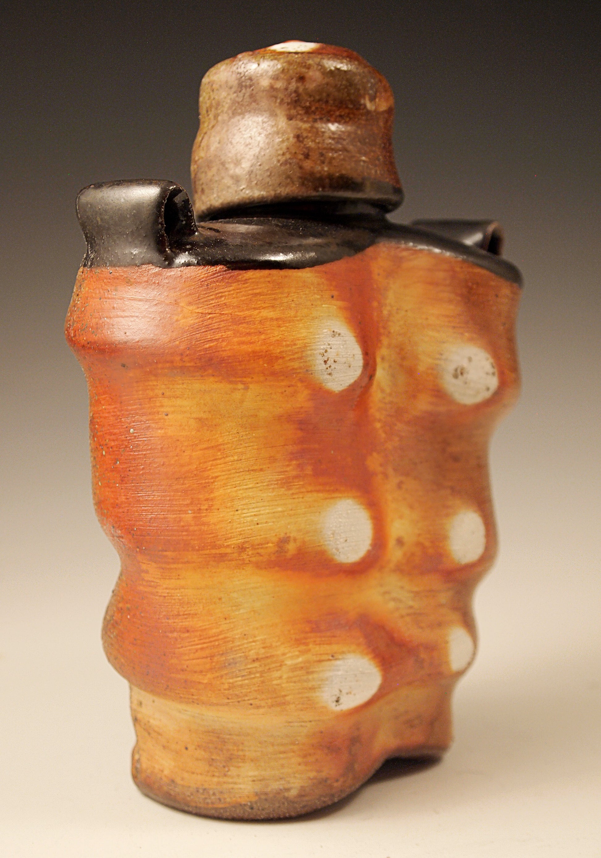 Wood-fired Stoneware Whiskey Flask with black liner glaze and black shoulders. Handmade. One-of-a-kind ceramic flask. 7" tall. 5.5" wide. 3" deep.  Side view.