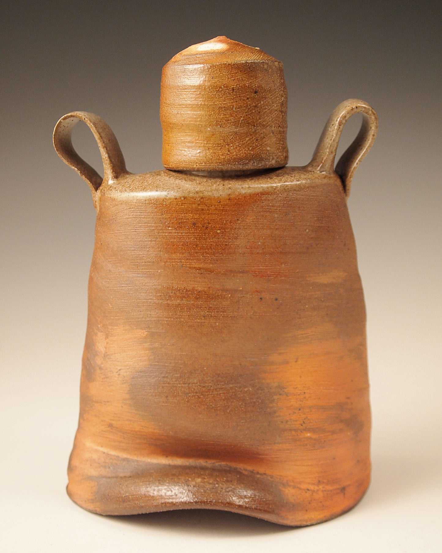 Small, handmade ceramic whiskey flask.  Wood-fired Stoneware.  Bright orange and brown slip exterior.  Rustic design. Back view.