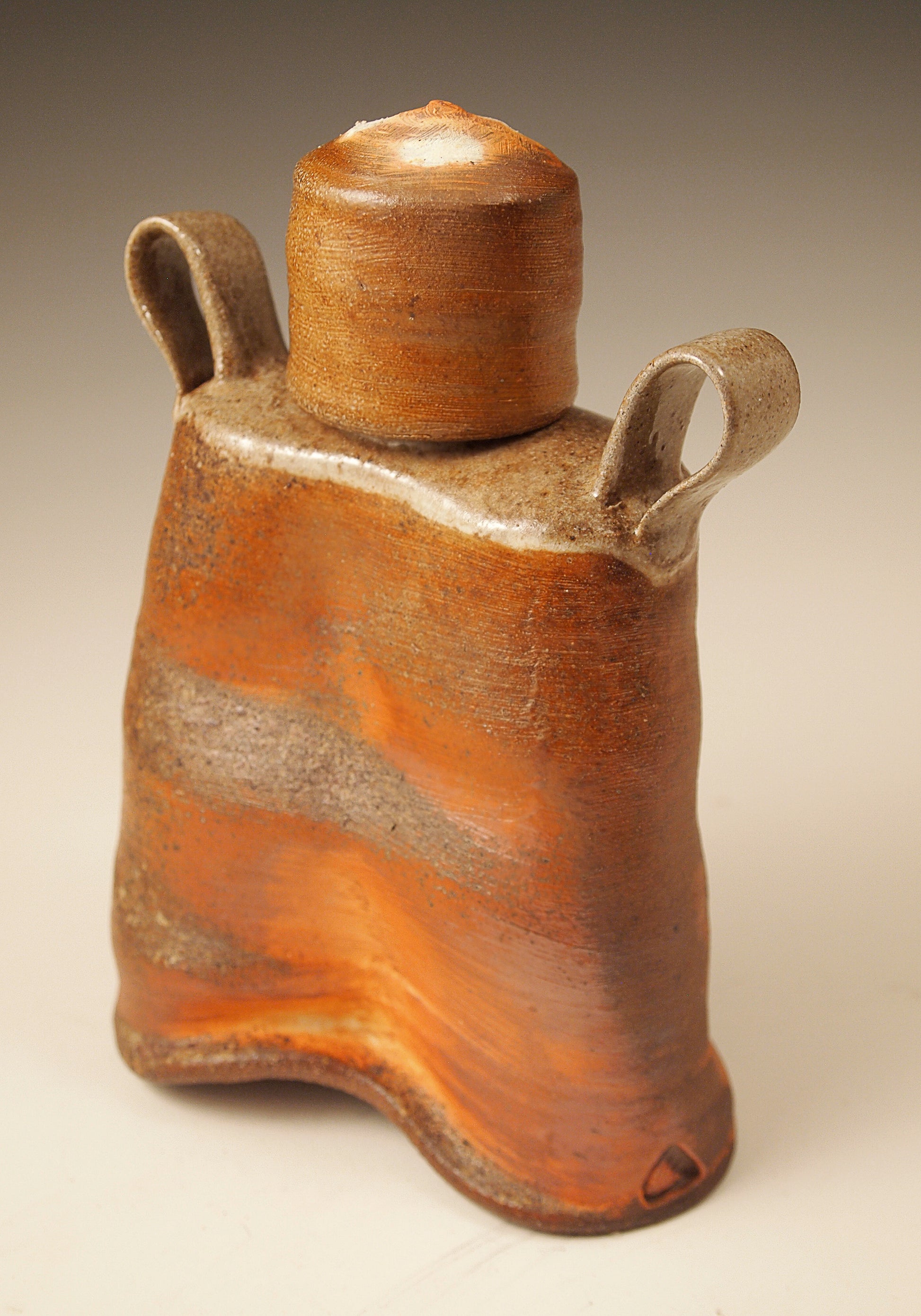 Small, handmade ceramic whiskey flask.  Wood-fired Stoneware.  Bright orange and brown slip exterior.  Rustic design.  View from an angle.